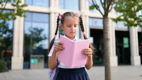 Smiling Schoolgirl Holding a Book in Front of School