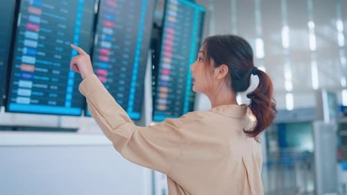 Happy asian woman traveler checking flight schedule board in airport terminal