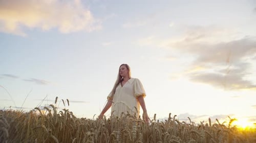 A Beautiful Caucasian Woman in a Dress is Standing in a Field of Wheat