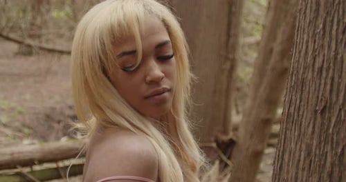 Black Girl With Blonde Hair, Wearing Pink Gown, Leans Against Tree In Forest. Close Up. Slow Motion