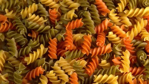 Pasta italiana multicolor Fusilli o Rotini, fondo giratorio, primer plano, vista superior, luz solar. Durum