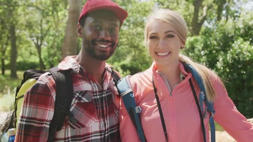 Portrait of happy diverse couple with backpacks embracing in park, slow motion