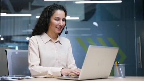 Woman Working on Laptop with Headset in Office