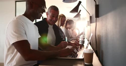 Junger afrikanischer Designer spricht mit einem reifen Kollegen und lacht während der Arbeit