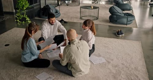 A Closeknit Team of Office Workers Discusses Data Reports While Sitting on a Carpet Brainstorming