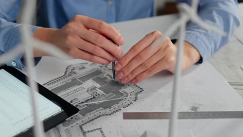 Un arquitecto se centra en los planos detallados del edificio mientras utiliza herramientas de dibujo y una tableta