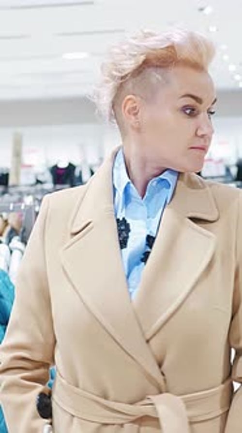 Stylish Woman in Beige Coat Browsing Clothing Racks in a Modern Retail Store Environment