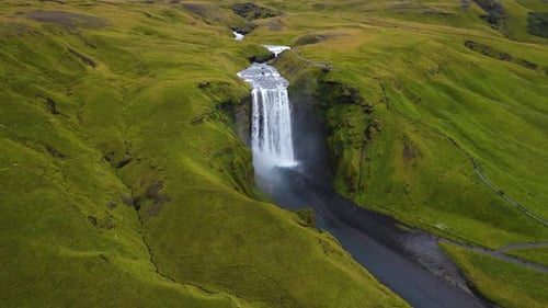 cinematic drone footage of Skógafoss Waterfall in Iceland, capturing the immense curtain of water