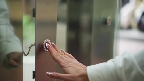 Nahaufnahme mit der Hand drückender Aufzugsknopf auf elegantem Metallpanel