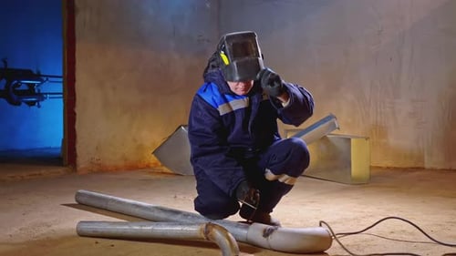 Man Welding Metal Piping in a Concrete Room