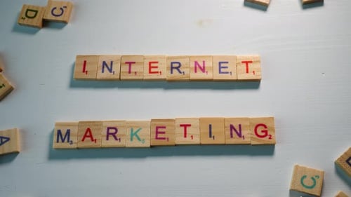 Someone spelling Internet Marketing with wooden letters on a table with other scattered letters. Whi