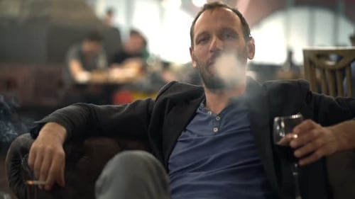 Porträt eines glücklichen Mannes, der im Café Addicted Zigarette raucht und Wein trinkt