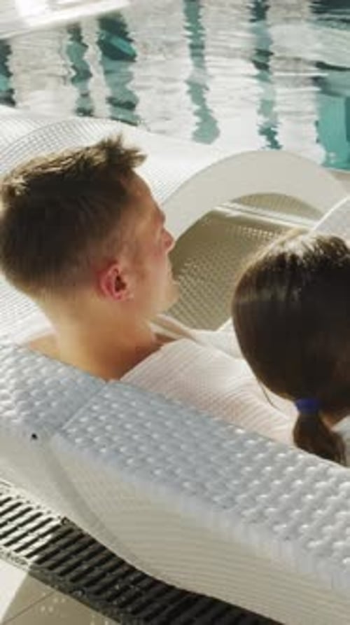 Young Couple Relaxing On Loungers by Poolside in Spa