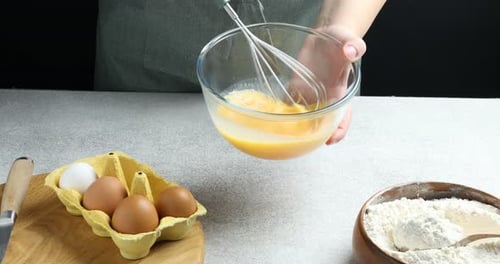 Woman whisking eggs in bowl at grey textured table against black background, closeup