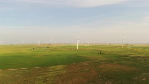 Wind farm in distant green fields, approaching drone shot with wind turbines