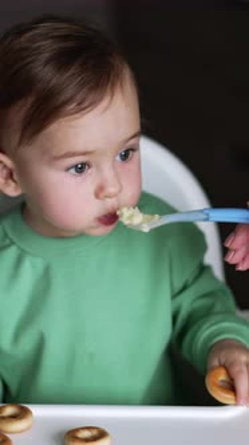 Infant Eating Meal with a Spoon in High Chair
