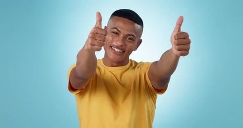 Face, smile and man with thumbs up, agreement and feedback with support on a blue studio background