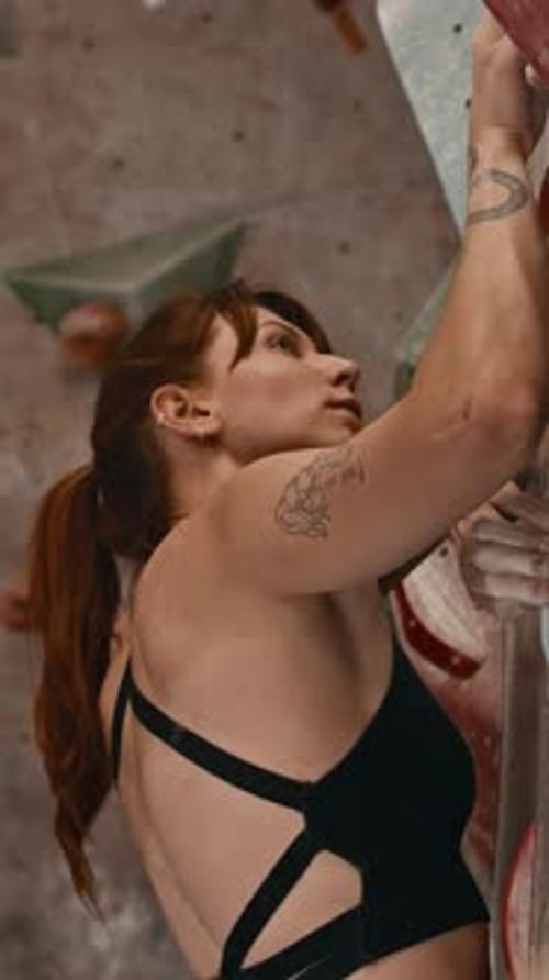 Vertical of Female Professional Climber Practicing in Indoor Bouldering Gym