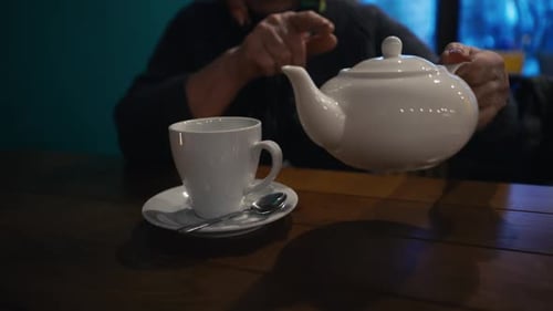 Person Pouring Tea into Cup at Cafe Table