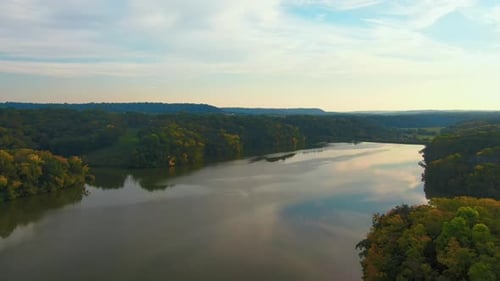 Majestätischer Drohnenflug über ein ruhiges Flusstal, umgeben von üppigem Wald zur Goldenen Stunde