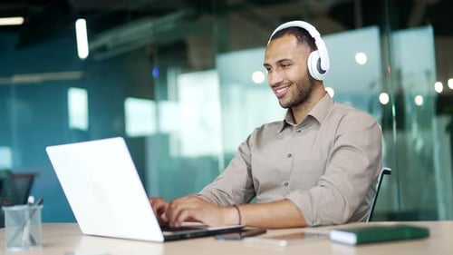 Man Types on Laptop Wearing Headphones in Office