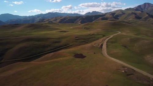 Drone footage captures a stunning panoramic view of mountainous terrain, winding roads, lush green h