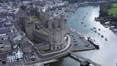 Ancient Caernarfon castle Welsh harbour town aerial view medieval waterfront landmark quick zoom out