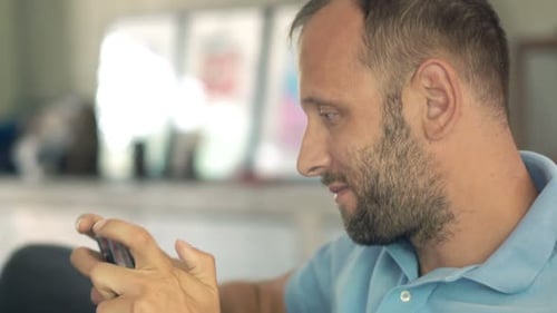 Man Uses Smartphone, Relaxing Indoors During the Day