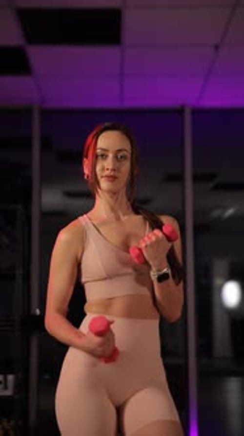 A Determined Young Girl Practices Strength Training with Dumbbells in a Stylish Night Gym Vertical