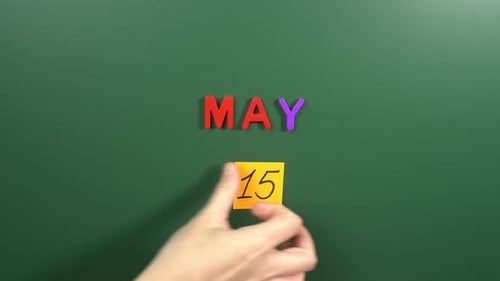 Hand sticking a sticker 15 May calendar day on school board. 15 date of May. Fifteenth day May