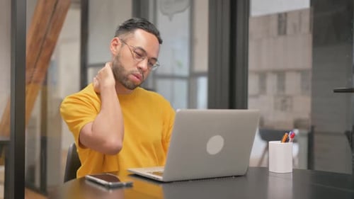 Young Man Working at Laptop, Rubs Neck