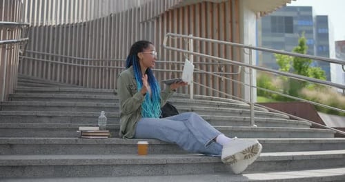 Woman Sits on Steps with Laptop Video Call