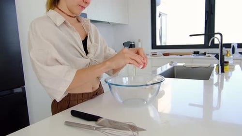 Woman Cracking Eggs into Bowl in Kitchen