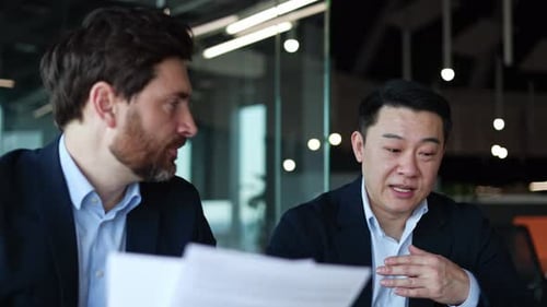 Two Serious Males Reading Sheets of Paper and Sharing Opinions in Workspace