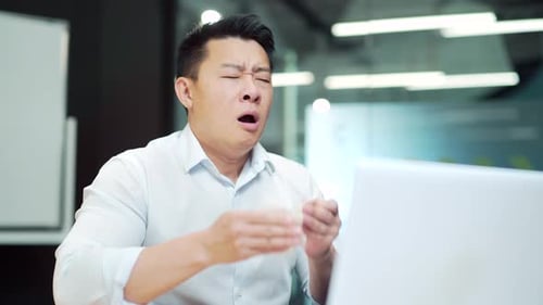 Man Blowing Nose While Working at Desk