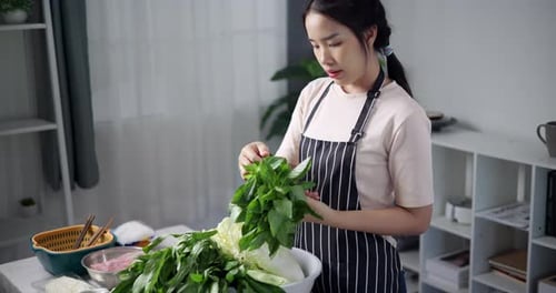 Asian woman is arranging vegetables in a bowl to prepare for cooking.