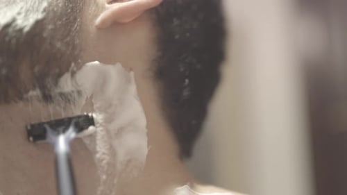 Homem branco de perto raspando a barba, banheiro, foto estática