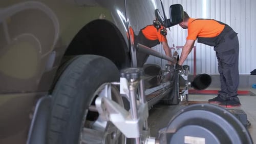 Two Men are Fixing a Car in a Garage Working on the Tire and Wheel