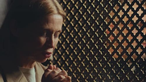 Woman Praying Silently in Dark Confessional