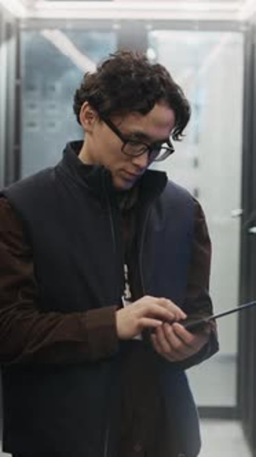Vertical Portrait of Asian Data Center Engineer Holding Tablet in Corridor