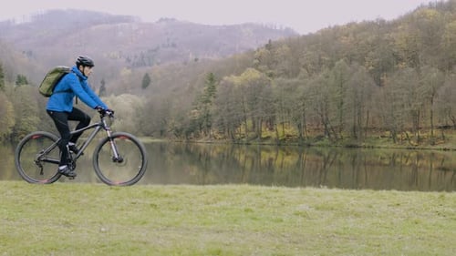 Young man biking freely through autumn forest beside still lake enjoying nature