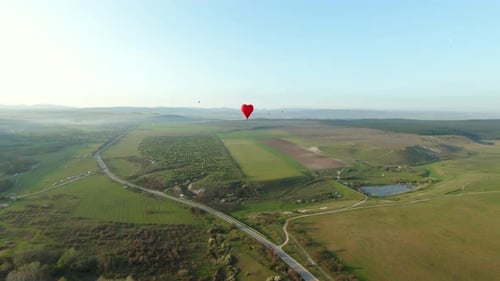 Red Heart Shaped Hot Air Balloon Flying Over Green Countryside