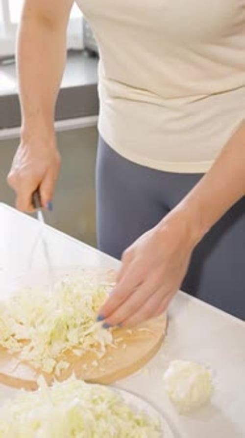 Vertical video. Woman Chopping Fresh Cabbage with Knife on Wooden Round Board in Kitchen, Concept