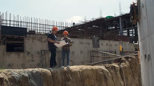 Construction manager and engineer discussing and checking plans on construction site.