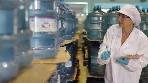 Jeune travailleuse heureuse dans une usine d'embouteillage vérifiant les bouteilles d'eau avant expédition. Qua d'inspection