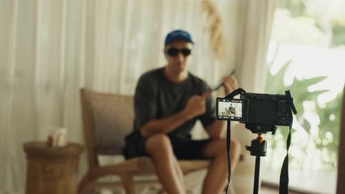 Man Sits Indoors, Speaks to Camera on Tripod