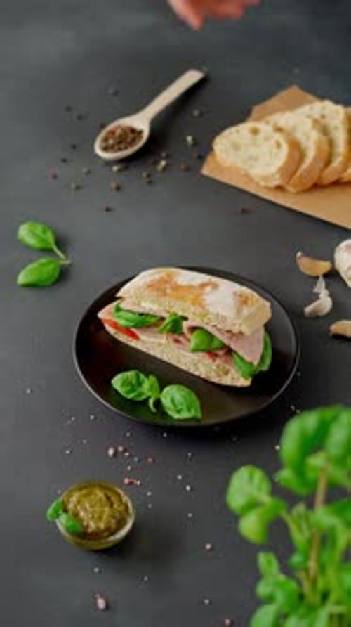 Men's hands pick up plate of Chiabatta Sandwich with ham, basil, pesto sauce, tomatoes from table