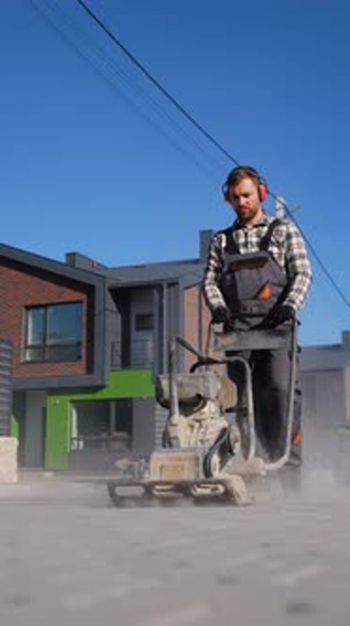 Worker Using Plate Compactor on Residential Pavement