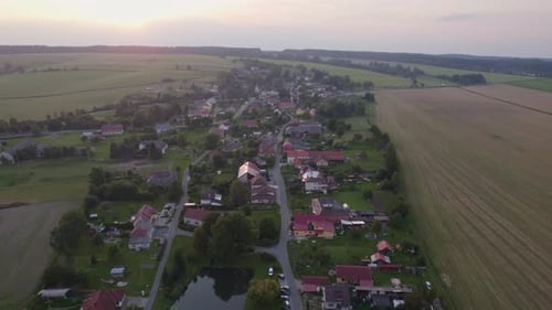 Slow drone flight over the village with houses and roads to the sunset in summer