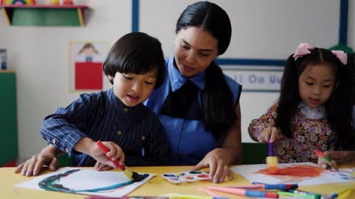 Maestra que ayuda a los niños en la clase de pintura en el aula de jardín de infantes. Niños y estudiantes multirraciales